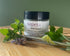 Jar of nepeta BSB Salve surrounded by green leaves and lavender on a wooden surface.