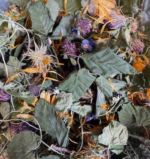 A close-up of dried herbal tea leaves and flowers, including red clover and birch leaf, commonly used in the product &